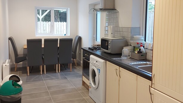 Cocina compacta con lavadora, microondas y zona de comedor con sillas.