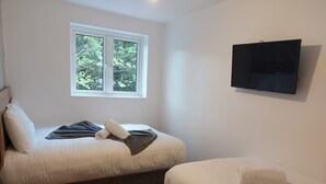 Un dormitorio con cama, ventana y televisor de pantalla plana en la pared.