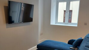 Una sala de estar moderna con un televisor de pantalla plana montado en la pared, un ventanal con vista a un edificio y un sofá seccional azul.