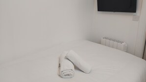 Habitación de hotel con cama, una toalla blanca enrollada, radiador blanco y televisor montado.