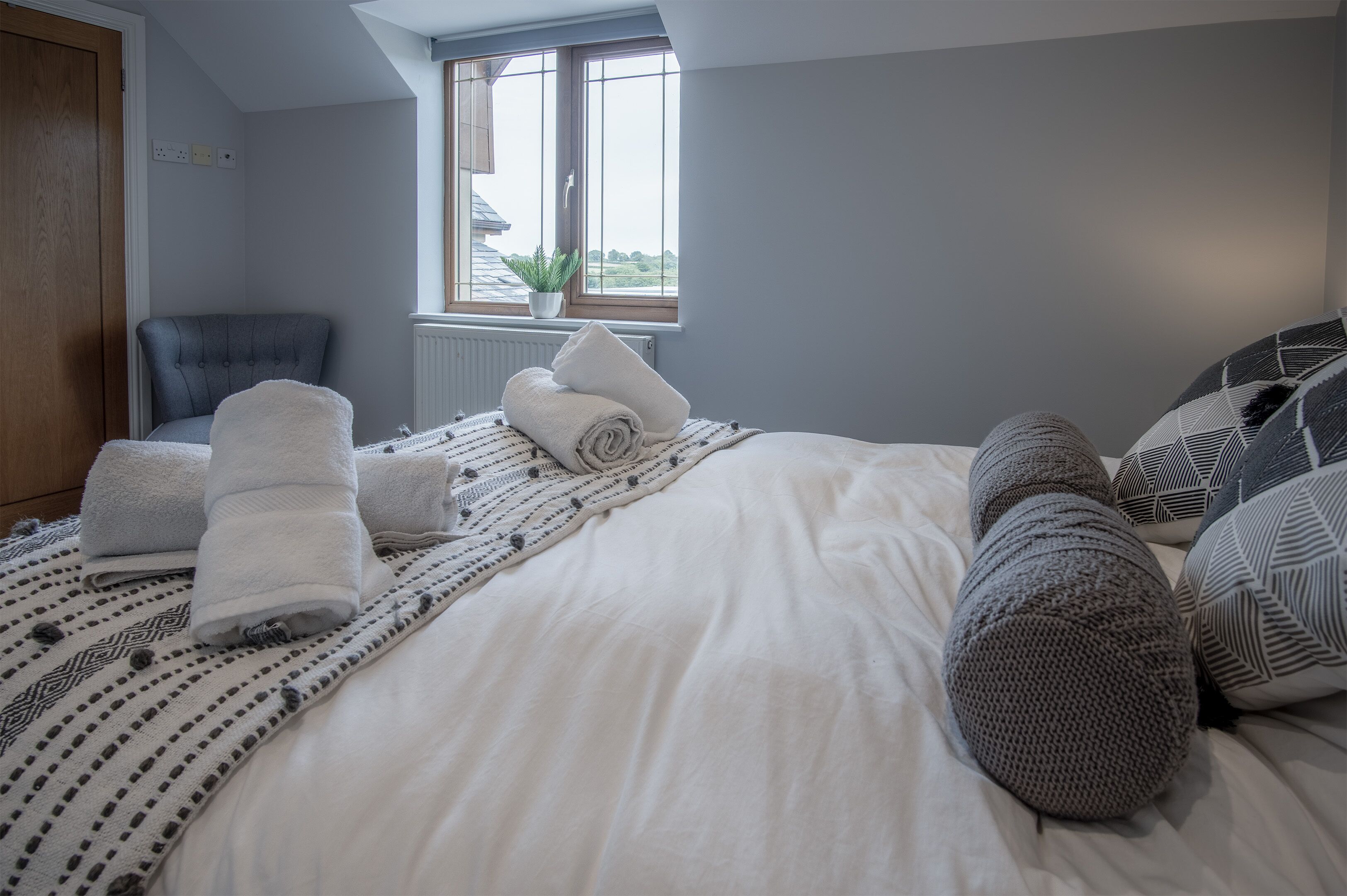A bedroom with a bed, pillows, a chair, a window, and a radiator.