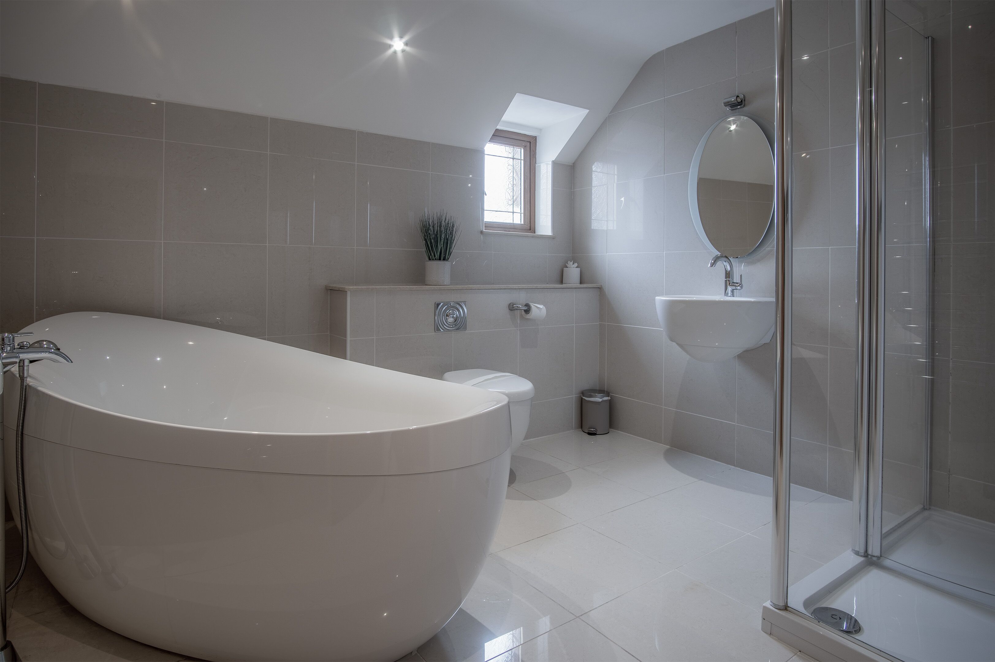 A modern bathroom with a freestanding bathtub, a shower enclosure, and a small window above the sink.