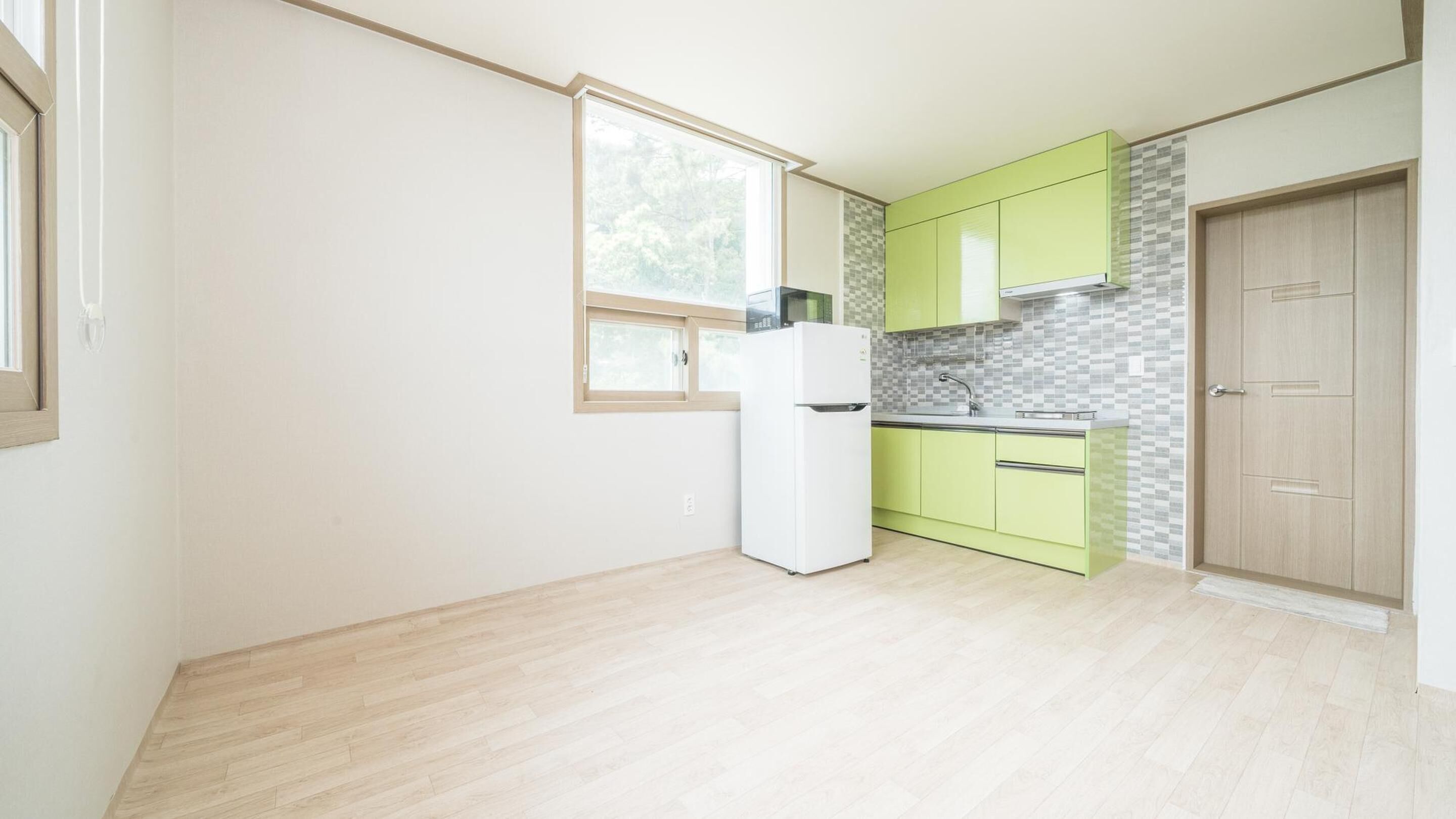 Une cuisine avec un réfrigérateur blanc, des armoires vertes, un pare-feu en carrelage et une porte en bois.