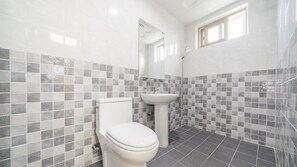 A bathroom with a toilet, sink, and shower. The walls are tiled with a checkered pattern.