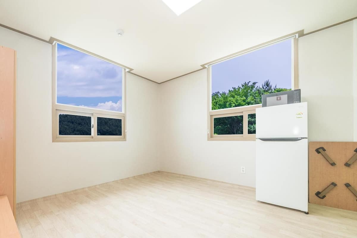 A spacious room with large windows, a white refrigerator, and a wooden floor.