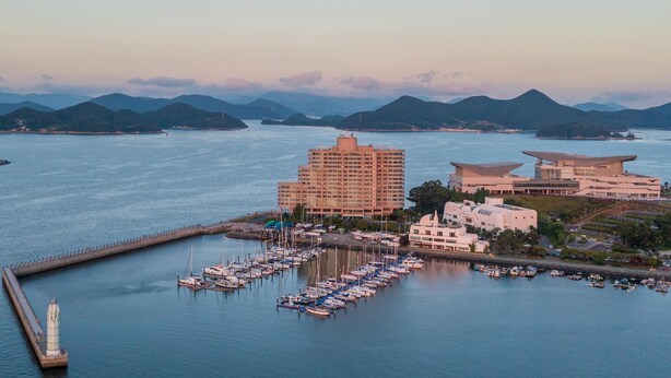 A marina with numerous boats docked, a large hotel building, and a distinctive modern building with a unique roof design. - Tongyoung Sandeulhae Healling Pension (Tongyeong)