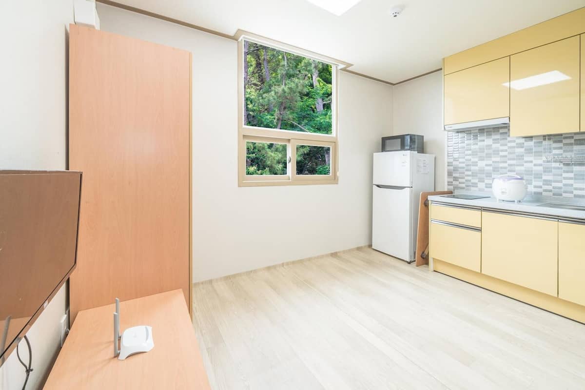 A compact kitchen with a refrigerator, microwave, and a window with a view of trees.