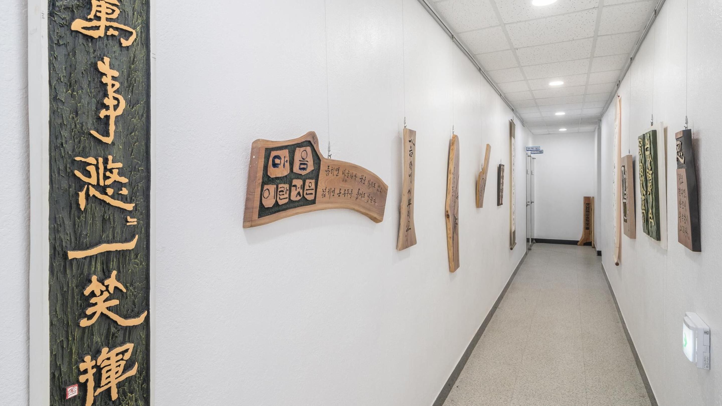 A hallway with artwork on the walls, a wooden sign with text, and a door at the end.