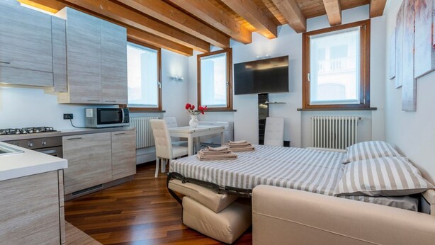 Una habitación compacta y moderna con kitchenette, una cama con ropa de cama a rayas, televisión y ventana con vistas.