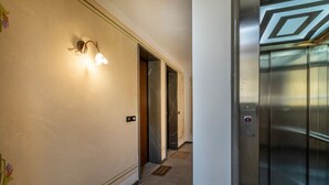 Un pasillo con una lámpara fijada a la pared, un ascensor y una puerta que da a otra habitación.