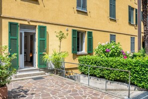 Un bâtiment avec des volets verts, une entrée pavée de pierres et une rambarde en métal.