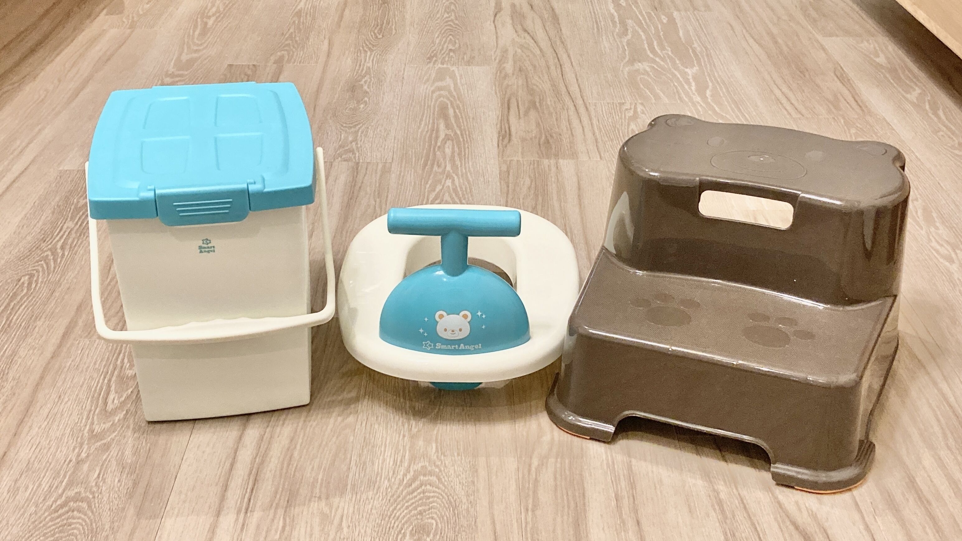 Three baby products: a white and blue storage bin, a blue and white baby potty, and a brown baby step stool.