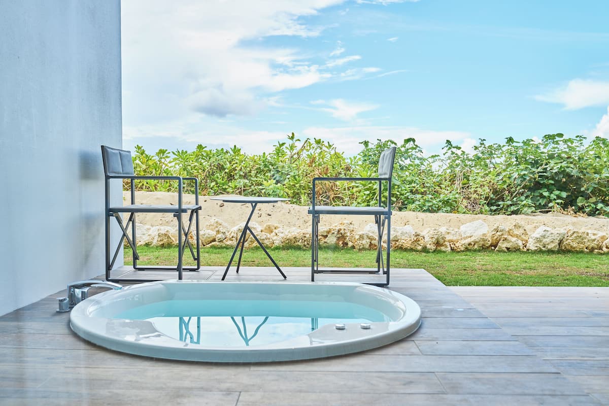 Ein moderner Poolbereich im Freien mit zwei Stühlen und einem Tisch, umgeben von einer Steinmauer und viel Grün.