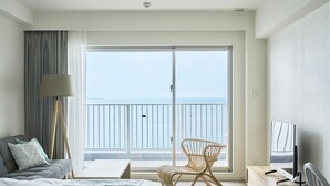 Habitación de hotel con cama, una silla, televisor y balcón con vista al mar.
