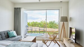 Una habitación de hotel moderna con un gran ventanal corredero que da a un balcón con hidromasaje, un sofá, una mesa de centro, un televisor y una lámpara.
