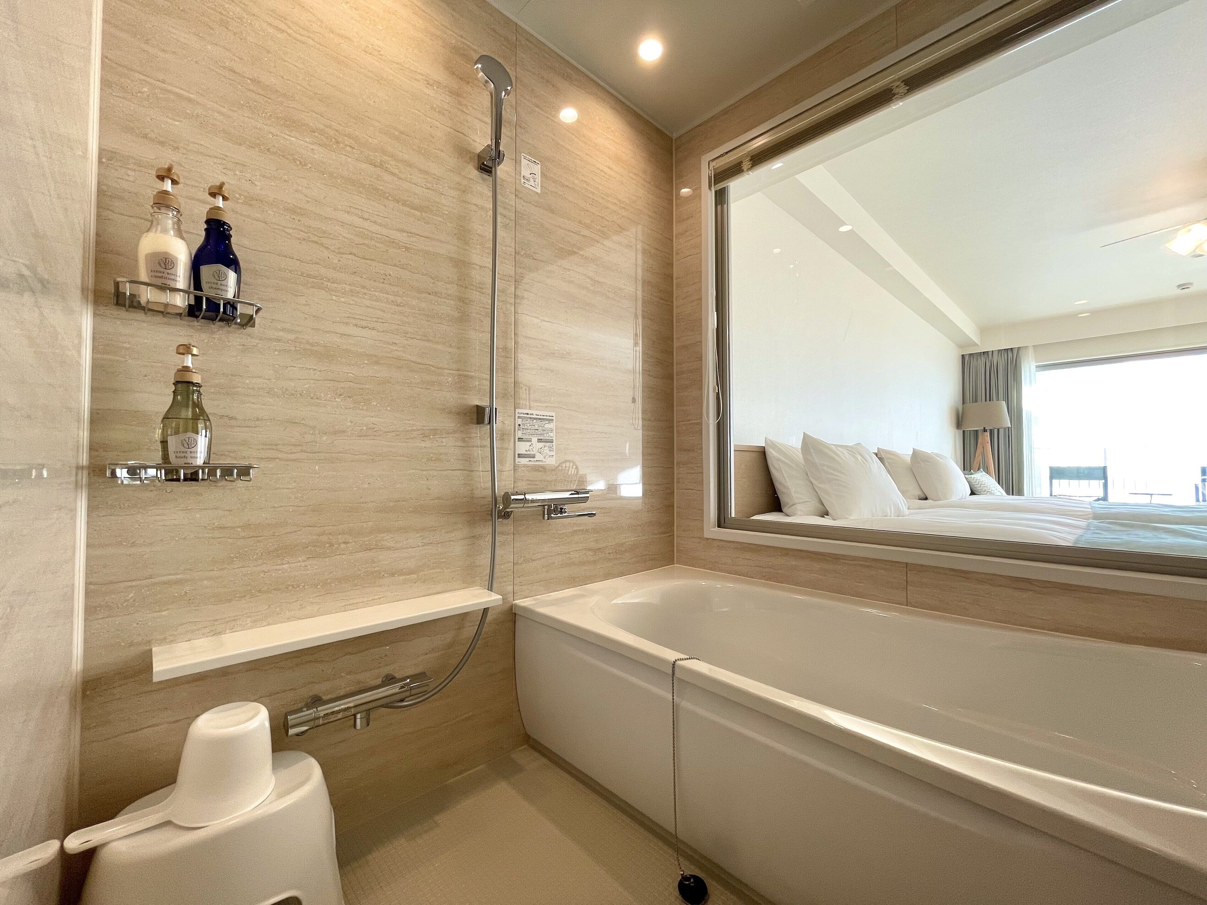 Une salle de bain moderne avec une baignoire, une douche et des toilettes. On trouve deux bouteilles de shampoing et d’après-shampoing sur une étagère.
