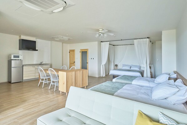 Una habitación de hotel moderna con cama, sofá, zona de comedor con sillas, microondas y pequeña cocina.