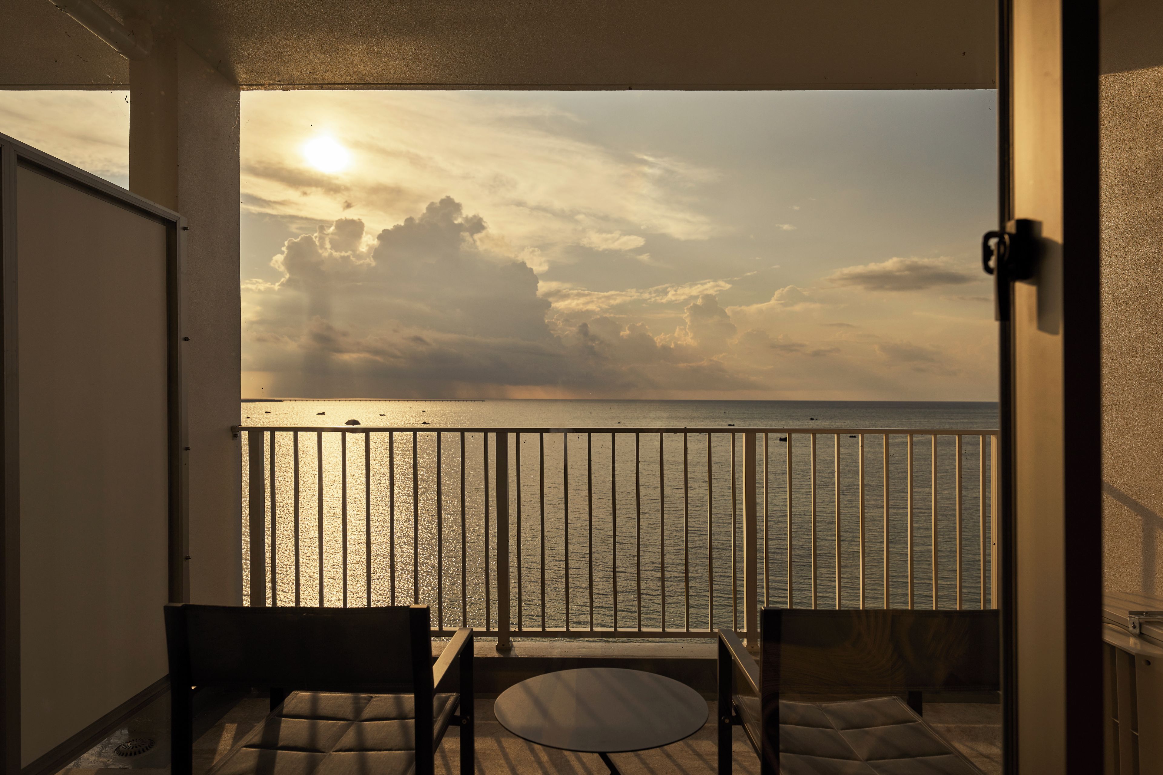 Un balcón con vista al mar, una silla y una mesa.