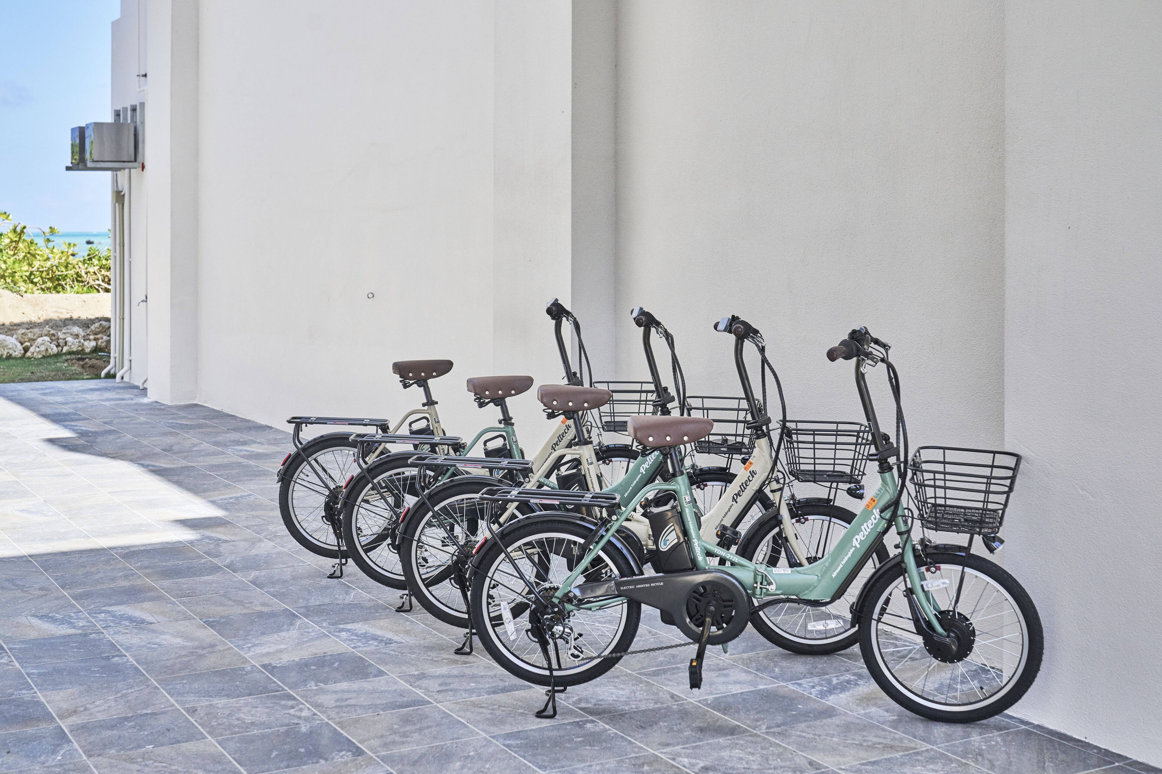 A row of electric bicycles parked against a wall with a tiled floor.