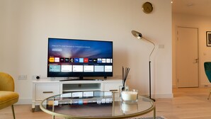 Ein modernes Wohnzimmer mit einem Flachbildfernseher auf einem Schrank, einem Glastisch und einer Stehlampe.
