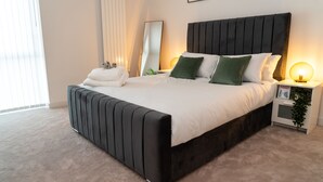 Ein modernes Schlafzimmer mit einem großen Bett, einem Nachttisch mit Lampe und einem Spiegel an der Wand.