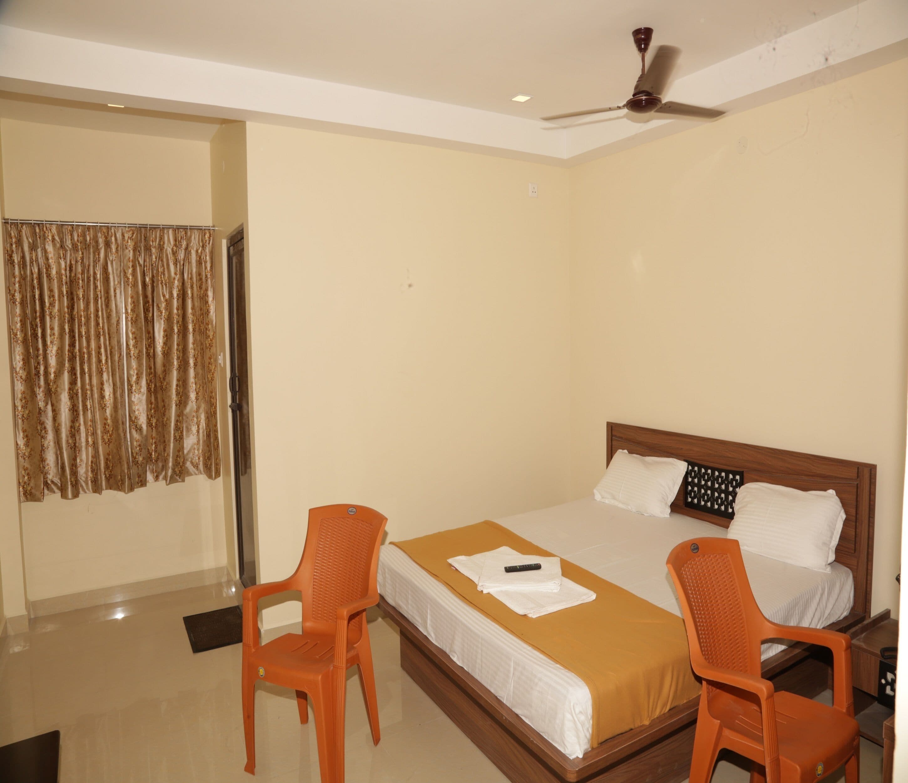 Habitación de hotel con cama, dos sillas, ventilador de techo y cortina.