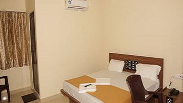 A hotel room with a bed, a desk, a chair, a ceiling fan, and an air conditioning unit.