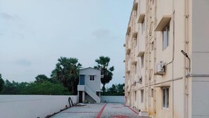 Un chemin pavé mène à un bâtiment à l’architecture moderne, avec un escalier et un mur blanc d’un côté.
