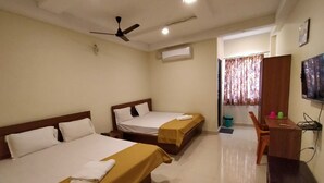 Une chambre d’hôtel avec deux lits, un bureau, une chaise, une télévision et un ventilateur de plafond.