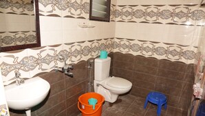 Une salle de bain avec un lavabo, des toilettes et une douche. On y trouve un tabouret bleu et un seau orange.