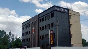 Un immeuble à plusieurs étages dont la façade porte l’inscription « SANTHOSH INN ».