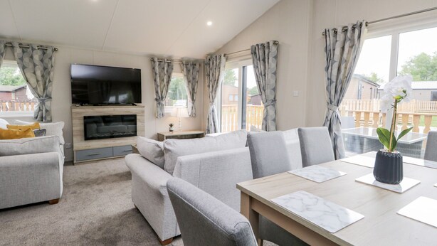 A modern living room with a flat-screen TV, grey sofas, a wooden coffee table, and a view of the outside deck. - Parkers Place (Carnforth)