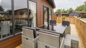 A wooden deck with a glass-enclosed patio area, furnished with wicker chairs and a table. - Parkers Place (Carnforth)