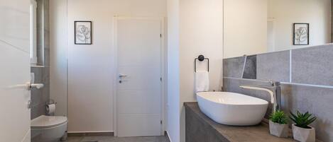 A modern bathroom with a white toilet, a large mirror, a white sink, and two small potted plants.