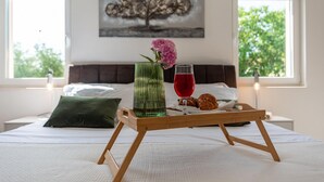 A bed with a tray of pastries and a glass of red drink, a green vase with flowers, and a painting of a tree on the wall. - Villa Dora Zadarvillas (Policnik)