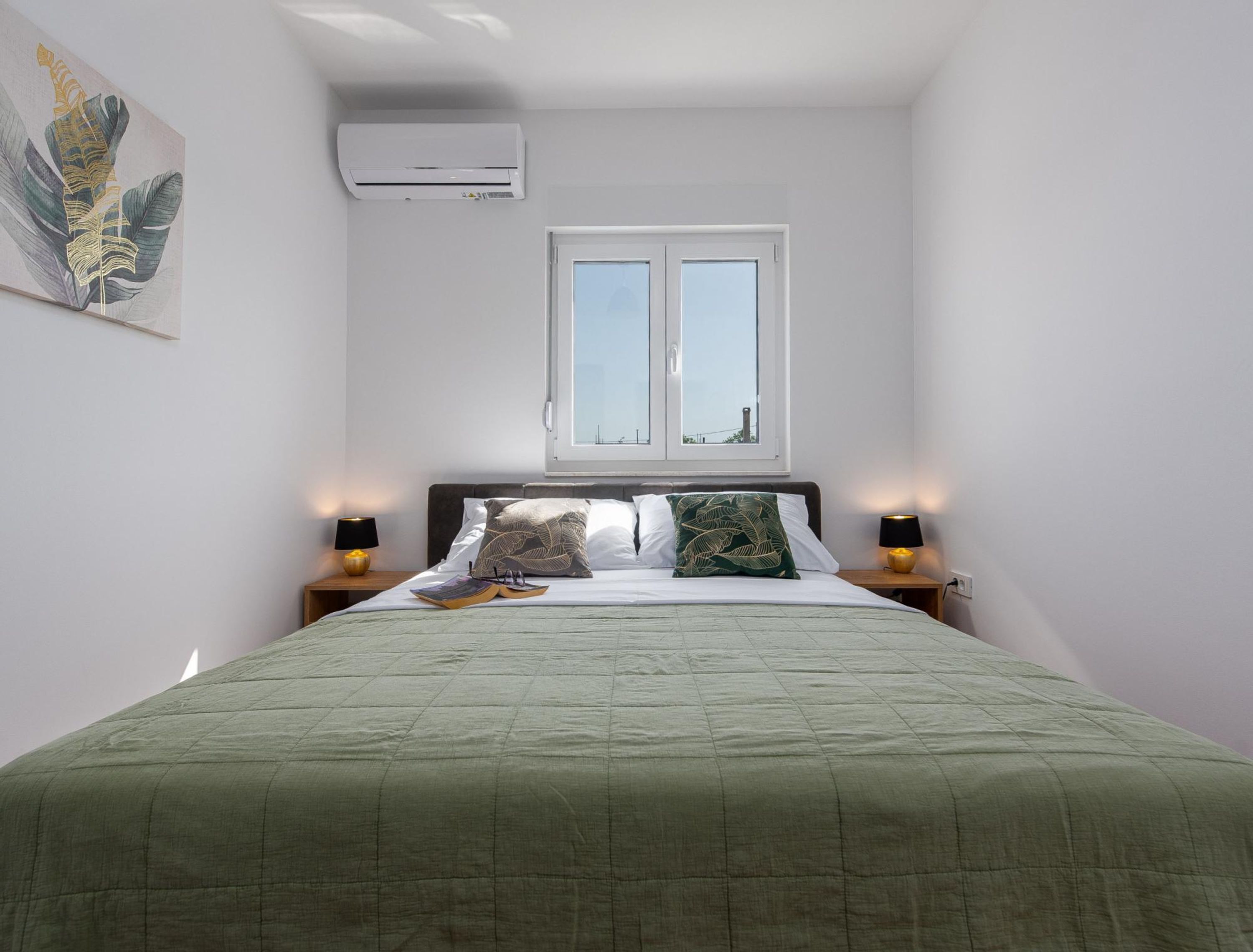 A bedroom with a bed, two bedside lamps, a window, and an air conditioner.