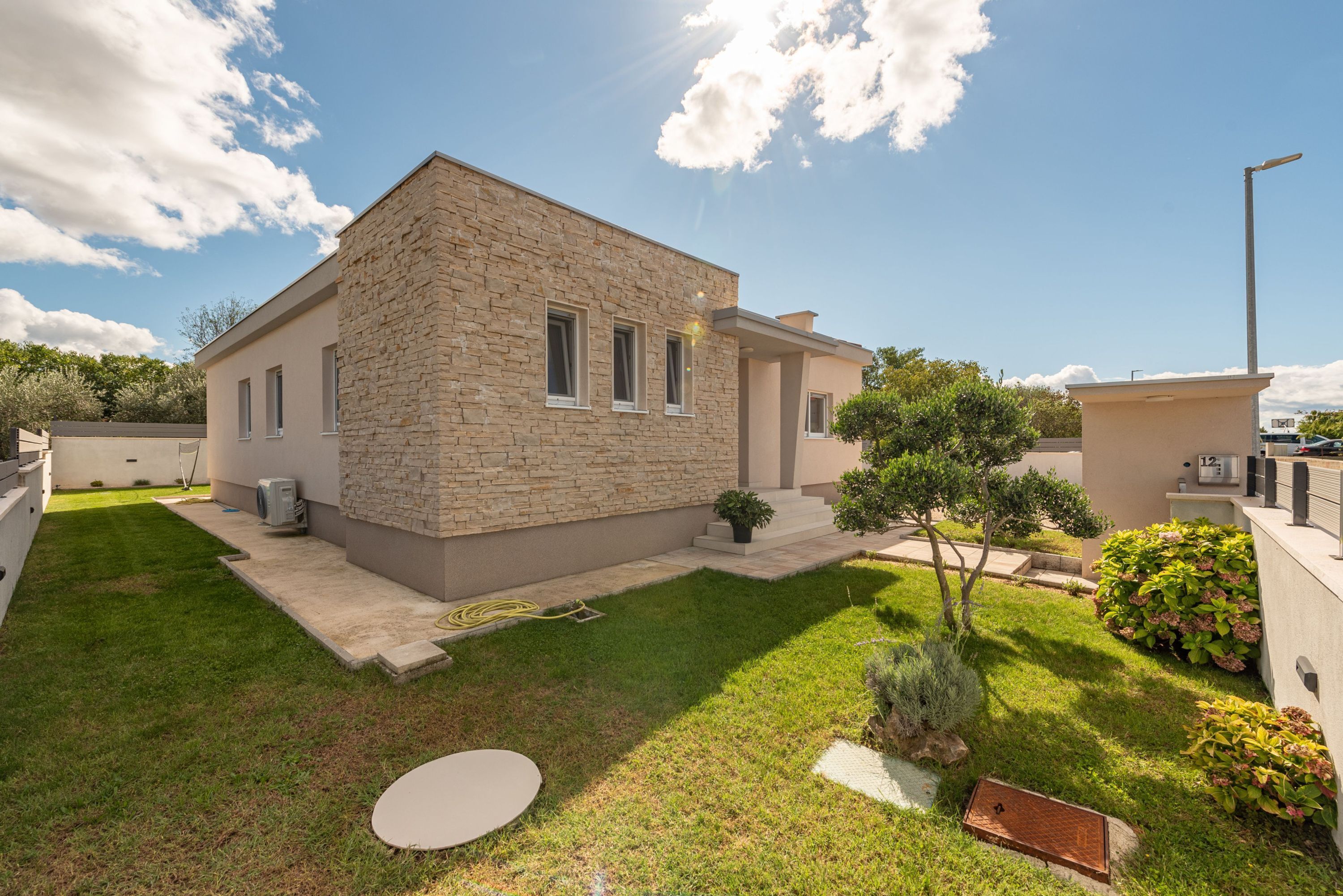 A modern house with a stone facade, a small garden with a lawn, and a paved patio area.