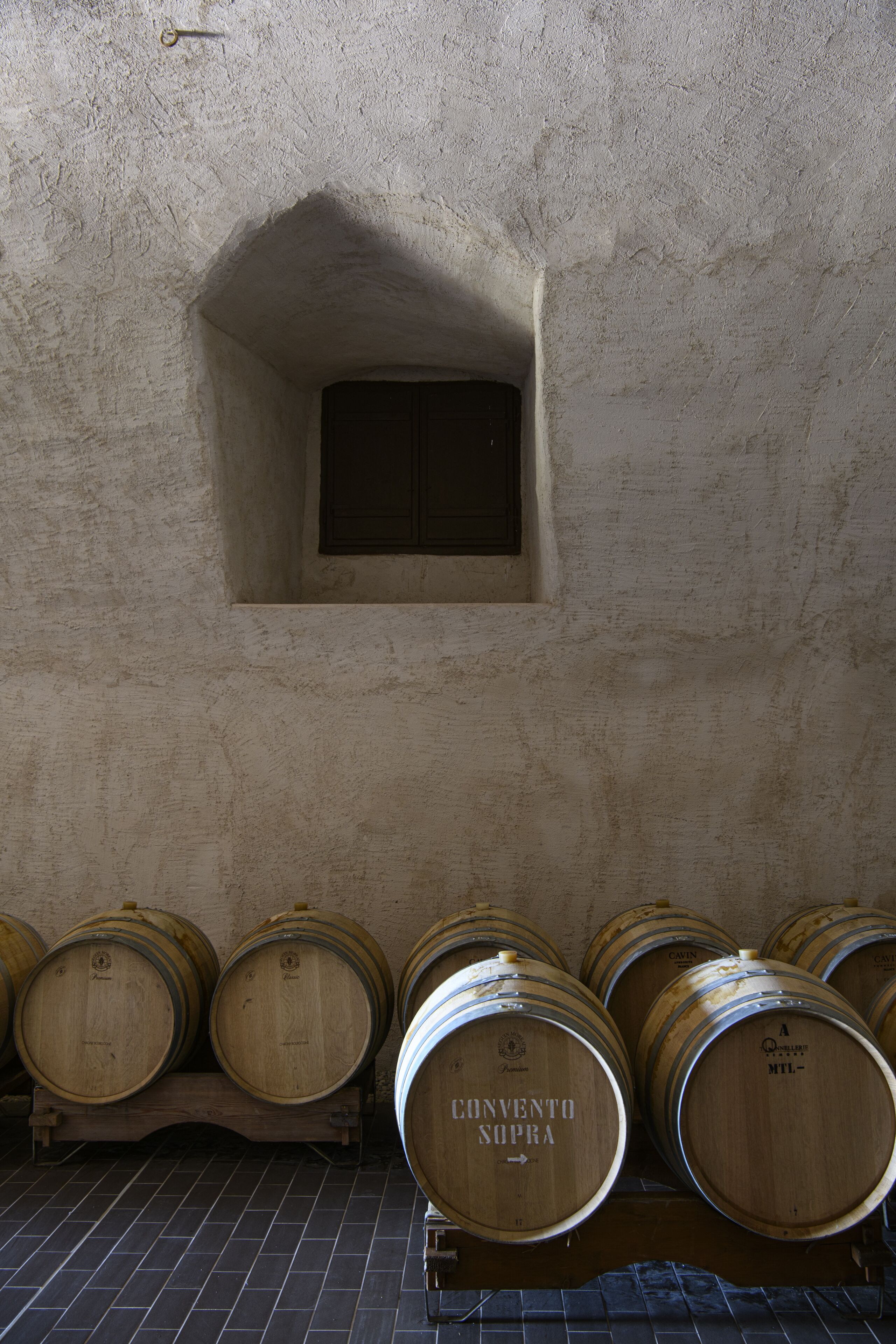 Wooden wine barrels in a cellar with a small window.