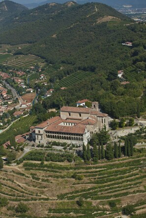 A large, historic building with a central courtyard, surrounded by terraced vineyards and a mountainous backdrop. - L'Annunciata Soul Retreat (Rovato)