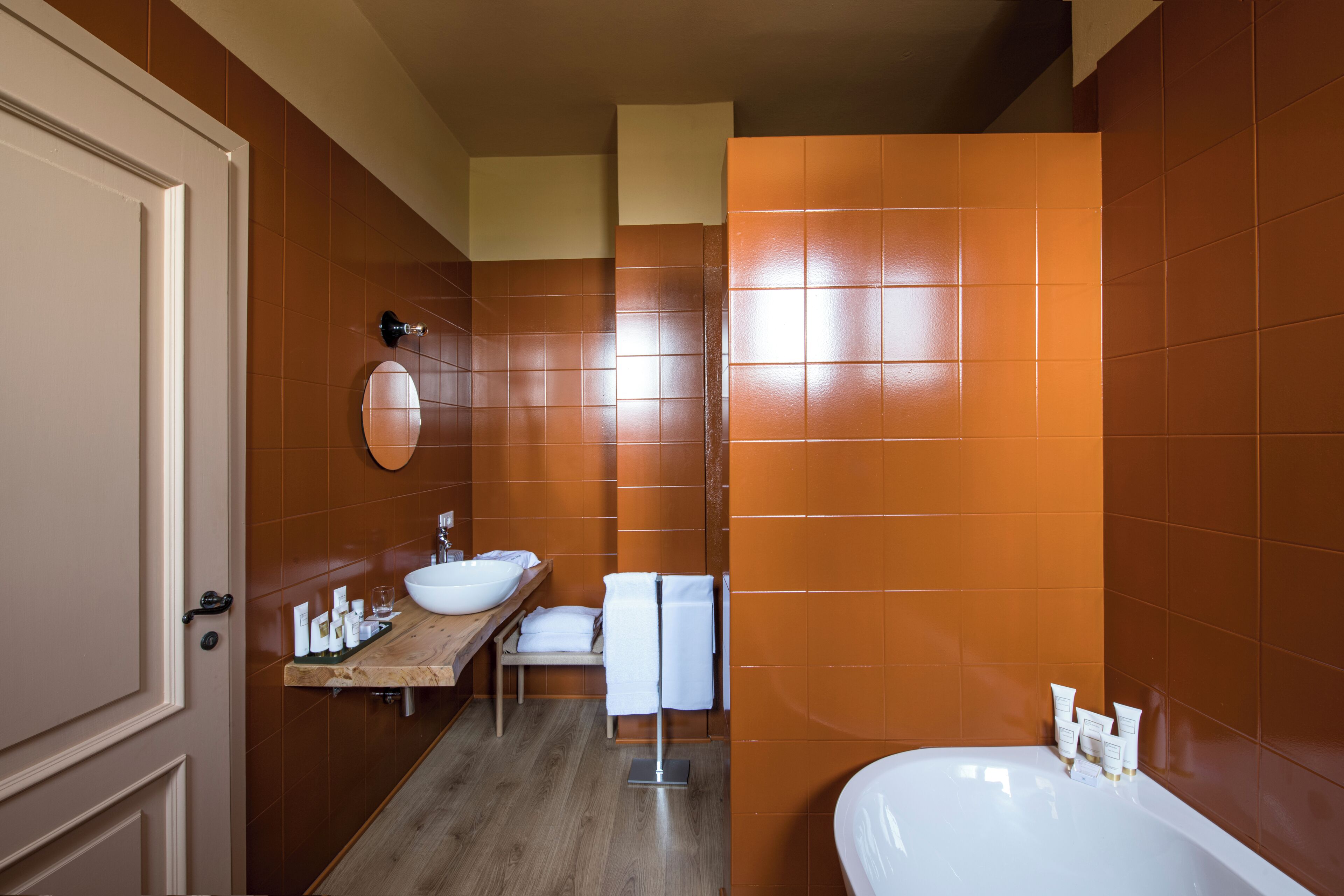 A modern bathroom with a wooden vanity, a large bathtub, and orange-tiled walls.