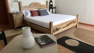 Une chambre à coucher bien rangée, avec un lit en bois, des lampes de chevet, une table de chevet sur laquelle repose un livre, un vase blanc et un tapis.