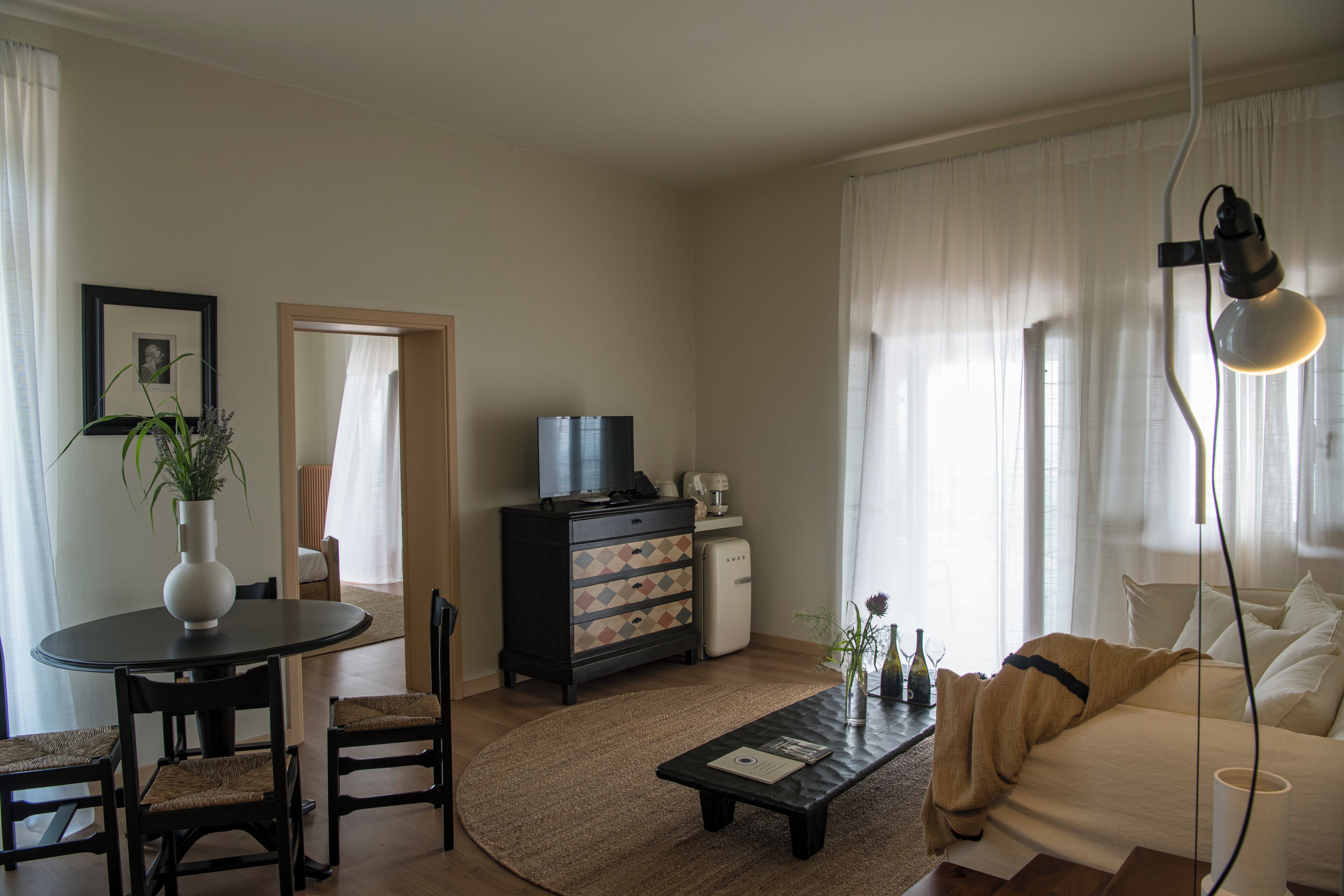 A living room with a sofa, coffee table, and a TV. There is a dining table with chairs and a plant.