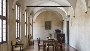 Een ruime hal met hoge plafonds en rondboogvensters, een eettafel met stoelen en een beeld aan de wand.