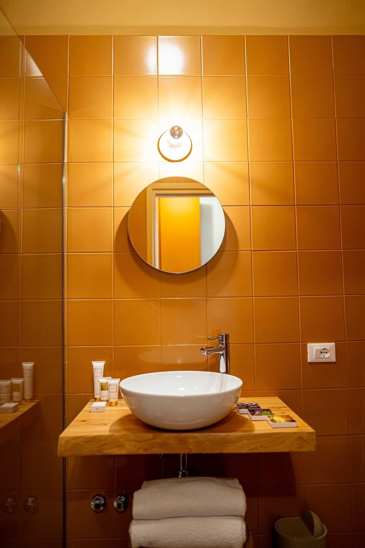 Ein Badezimmer mit einem weißen Waschbecken, einem runden Spiegel und einer Holzablage.
