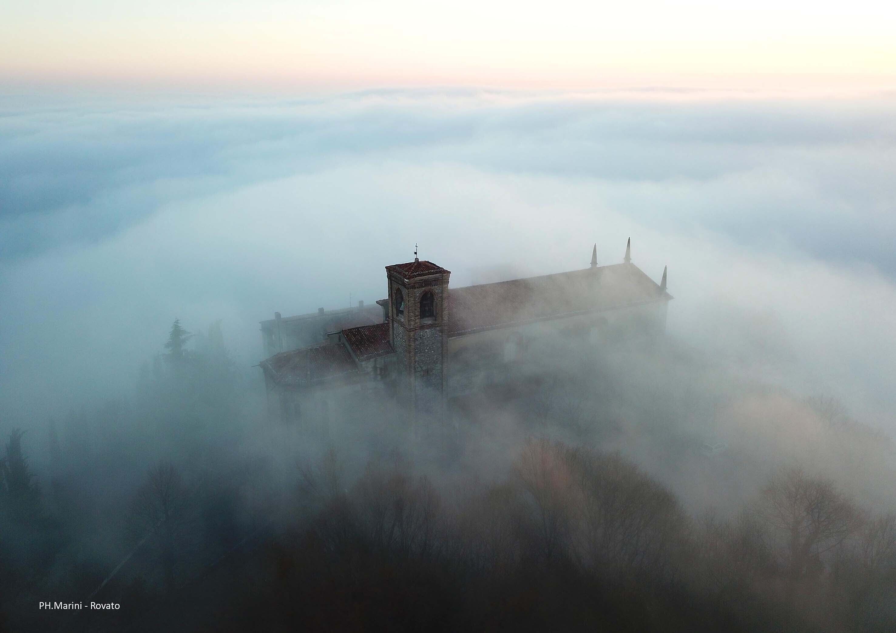 Un edificio histórico con un campanario, rodeado de densa niebla.