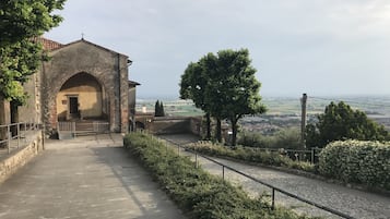 Un sendero conduce a un edificio histórico con una entrada en arco, rodeado de follaje y con vistas a un paisaje lejano.