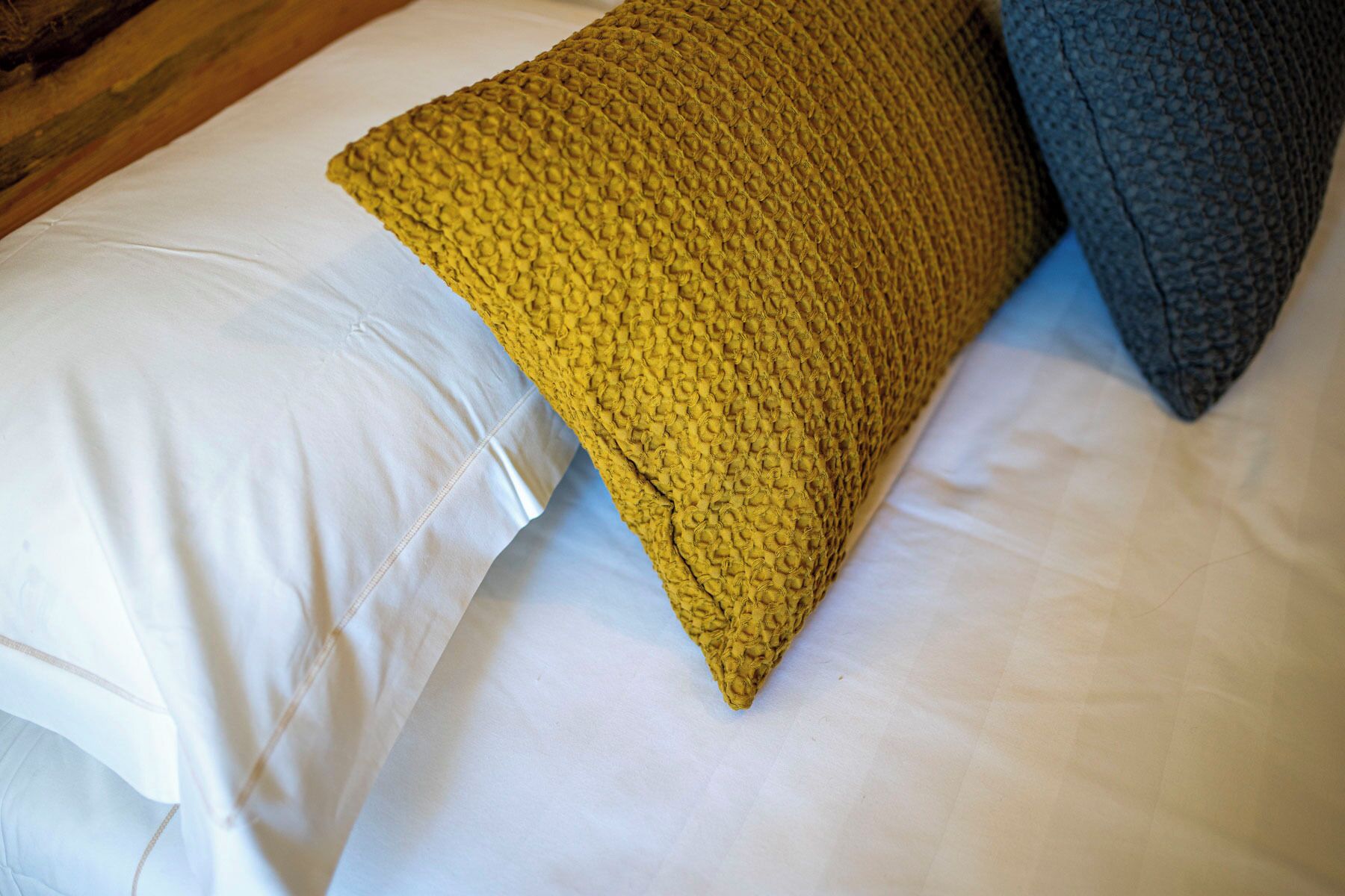 A bed with white sheets and two pillows, one yellow and one dark blue.