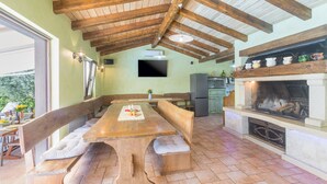A wooden dining table with benches, a television mounted on the wall, and a fireplace with decorative items. - Pool, whirlpool, 12 persons, garden, children's playground,bicycles,table tennis (Anžici)