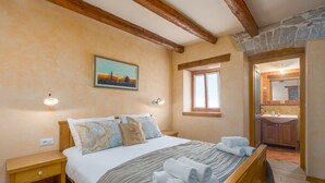 A bedroom with a wooden bed, a nightstand, a painting on the wall, and a view to the bathroom. - Pool, whirlpool, 12 persons, garden, children's playground,bicycles,table tennis (Anžici)