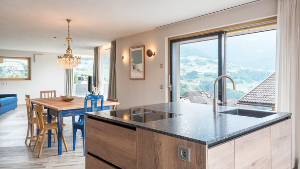 Una cocina moderna con una isla grande, un comedor con sillas de madera y vistas al campo a través de amplios ventanales.